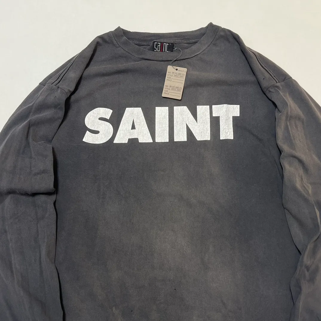 SAINT Mxxxxxx S>N>T LS TEE/BLACK Autumn and winter new style S>N>T slogan crack printed long TEE, washed black S-XL Asut ready-made garments dyed, the whole piece sprayed with horse-hair spray, and then sprayed again to fade the color. The collar and cuffs are frayed. Many hangings are worn NEW VINTAGE. Heavy craftsmanship.